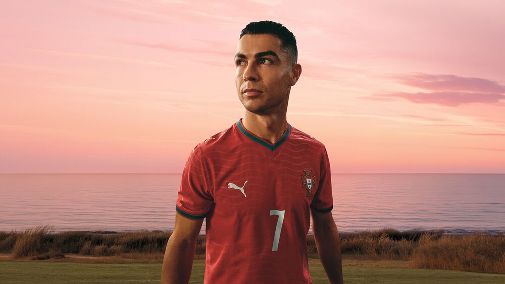 Ronaldo in home jersey with Puma logo, kicking a soccer ball against a pink sky.